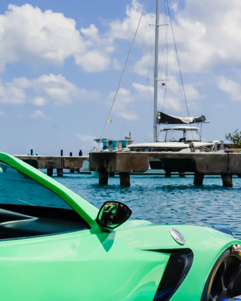 Green sports car near sailboat on sunny dock