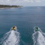 Two boats speeding on clear blue water near coast